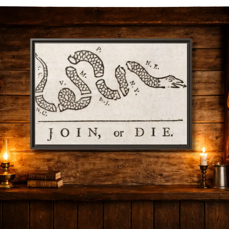 Join, or Die framed canvas hung on a rustic wooden plank wall above a shelf with leather-bound books, an oil lamp, and a lit candle