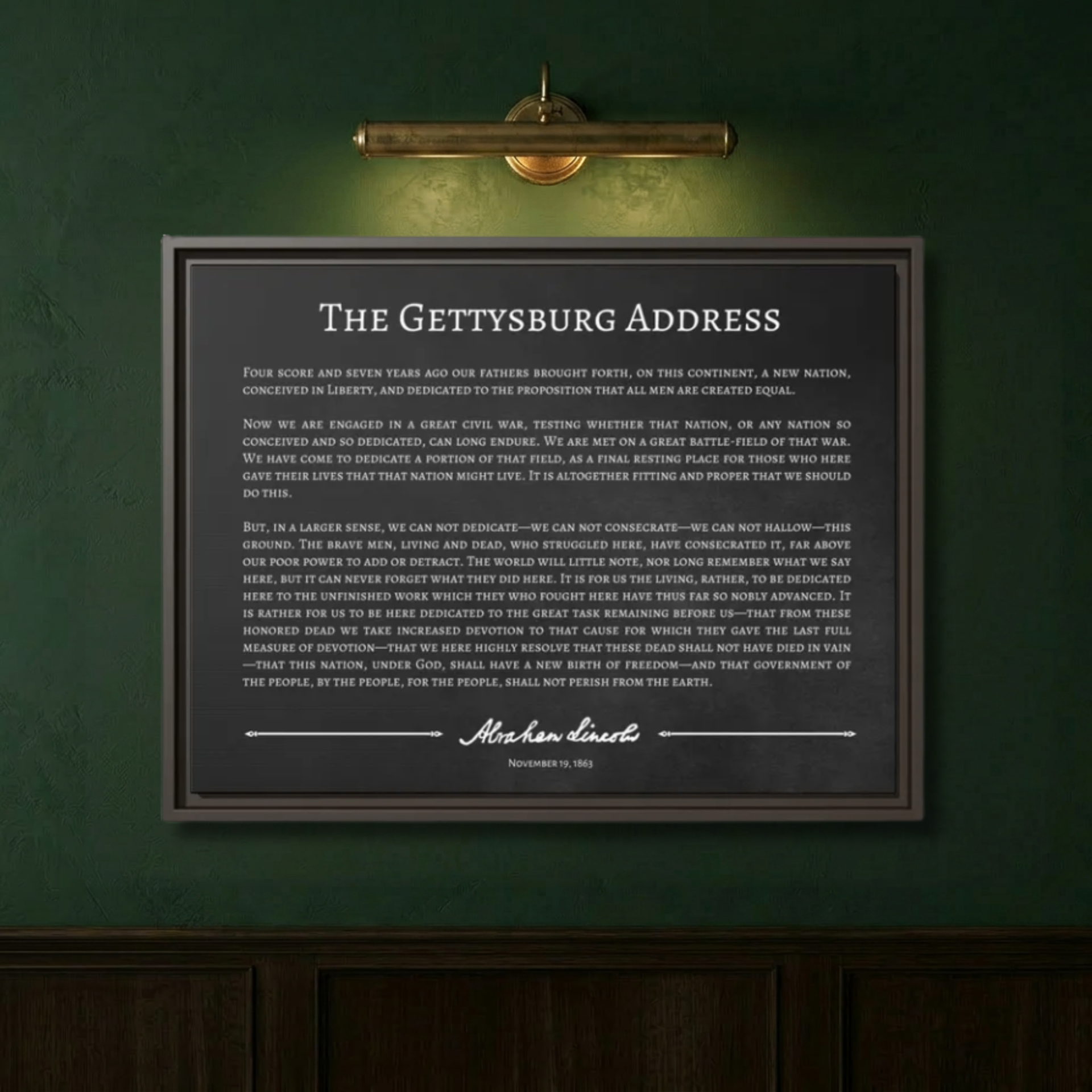 Close-up of the Gettysburg Address framed canvas on a deep sage green wall lit by a brass picture light